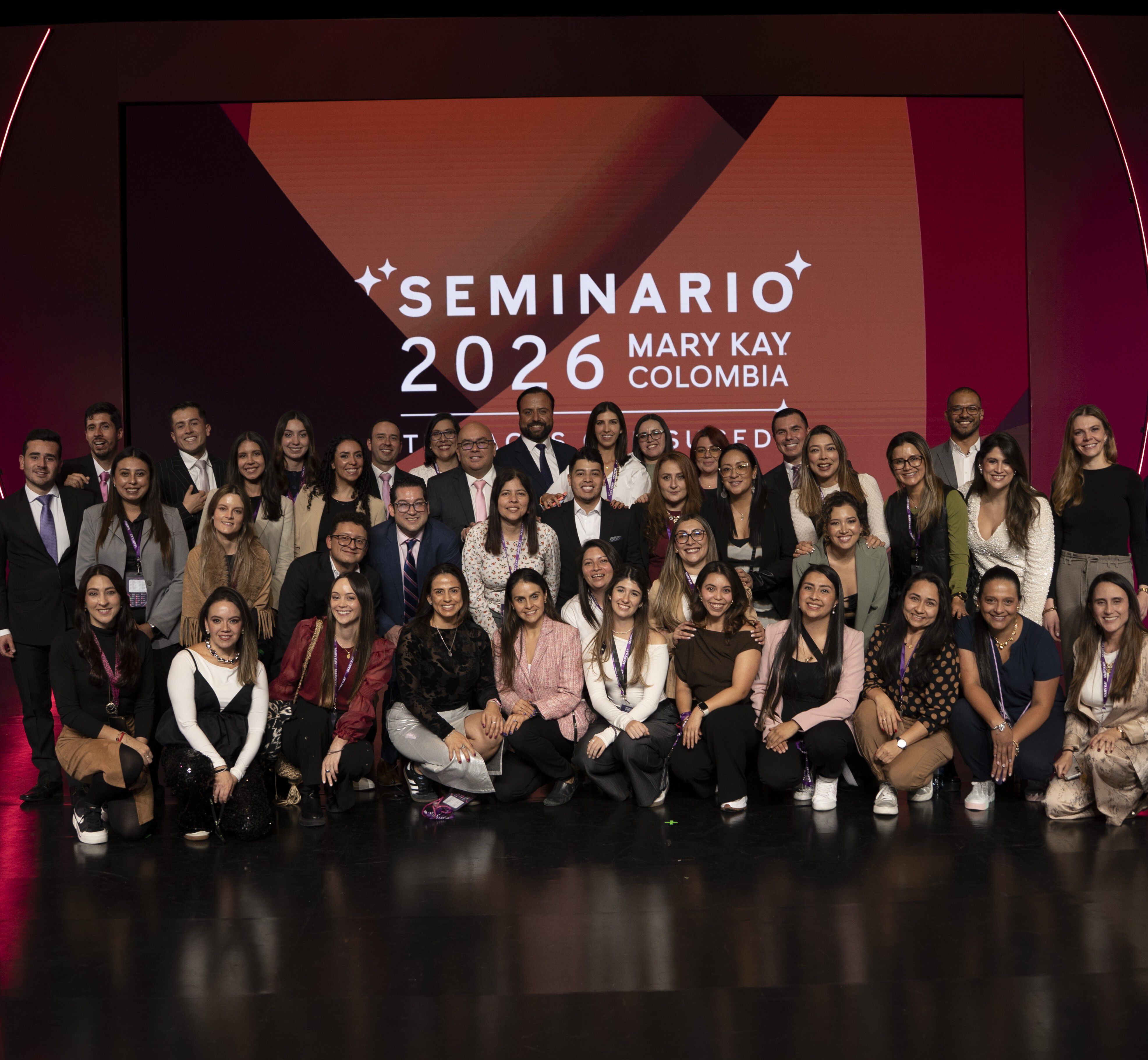 Tres colaboradores de Mary Kay trabajando en equipo alrededor de una mesa, con productos para el cuidado de la piel, una laptop y bocetos de dise&ntilde;o.