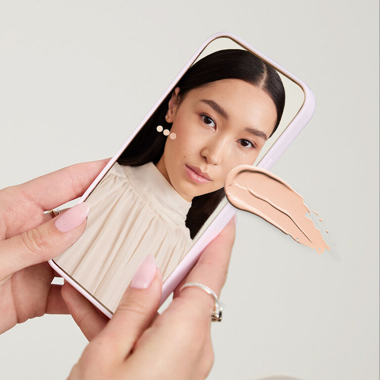Manos sosteniendo un dispositivo m&oacute;vil que muestra la herramienta Tu Tono Ideal de Mary Kay. 